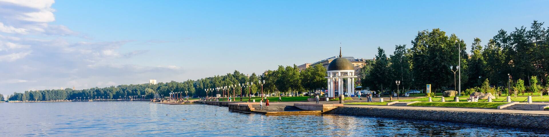A calm lake with a gazebo, trees, and a distant building.