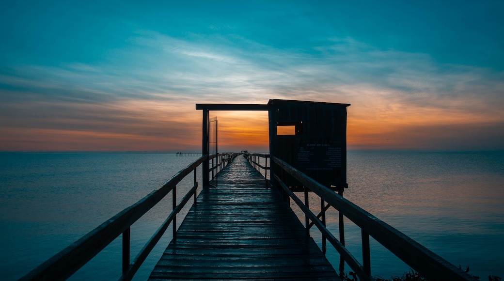 A wooden pier extending into calm waters at sunset.