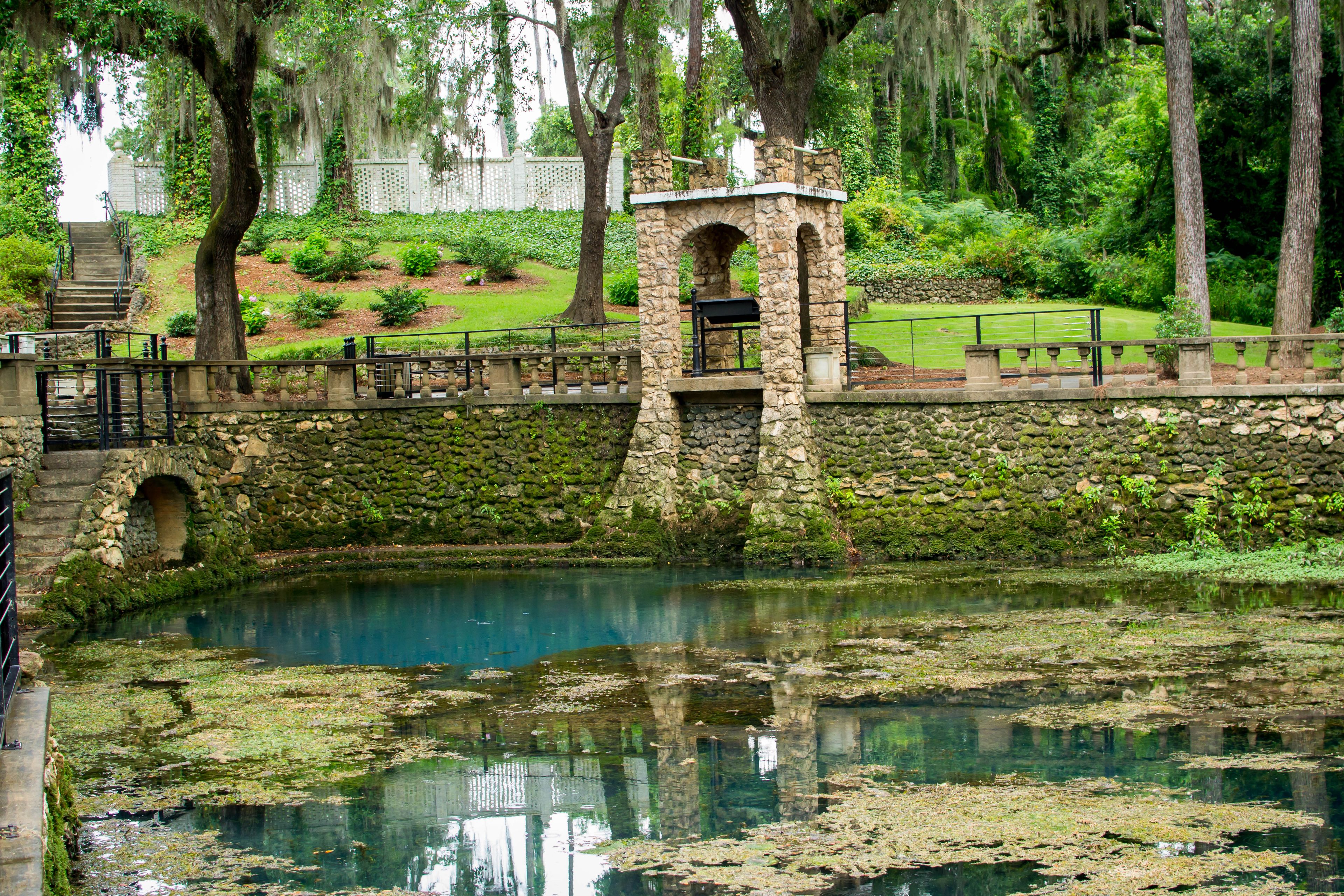 A stone bridge over a pond with moss-covered walls and a statue on top.
