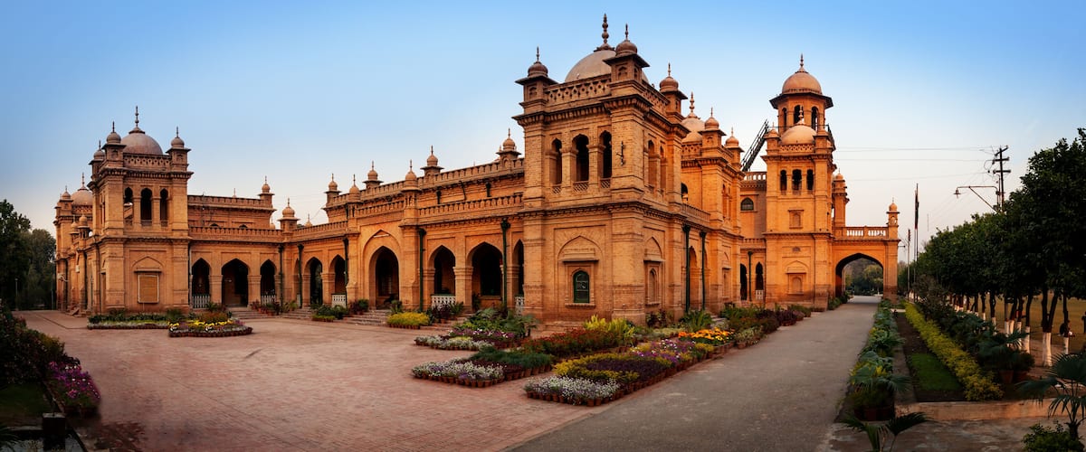 A large, ornate building with multiple domes and arches, surrounded by a well-maintained garden with various flowering plants.
