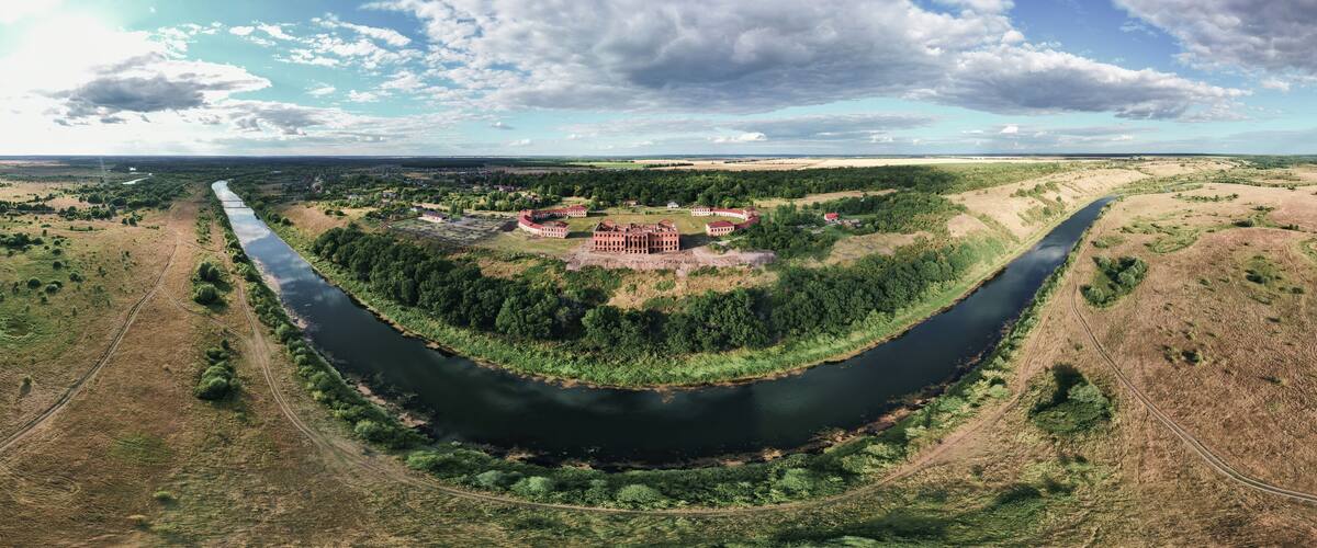 An aerial view of a river curving through a landscape with a cluster of red-roofed buildings surrounded by greenery.