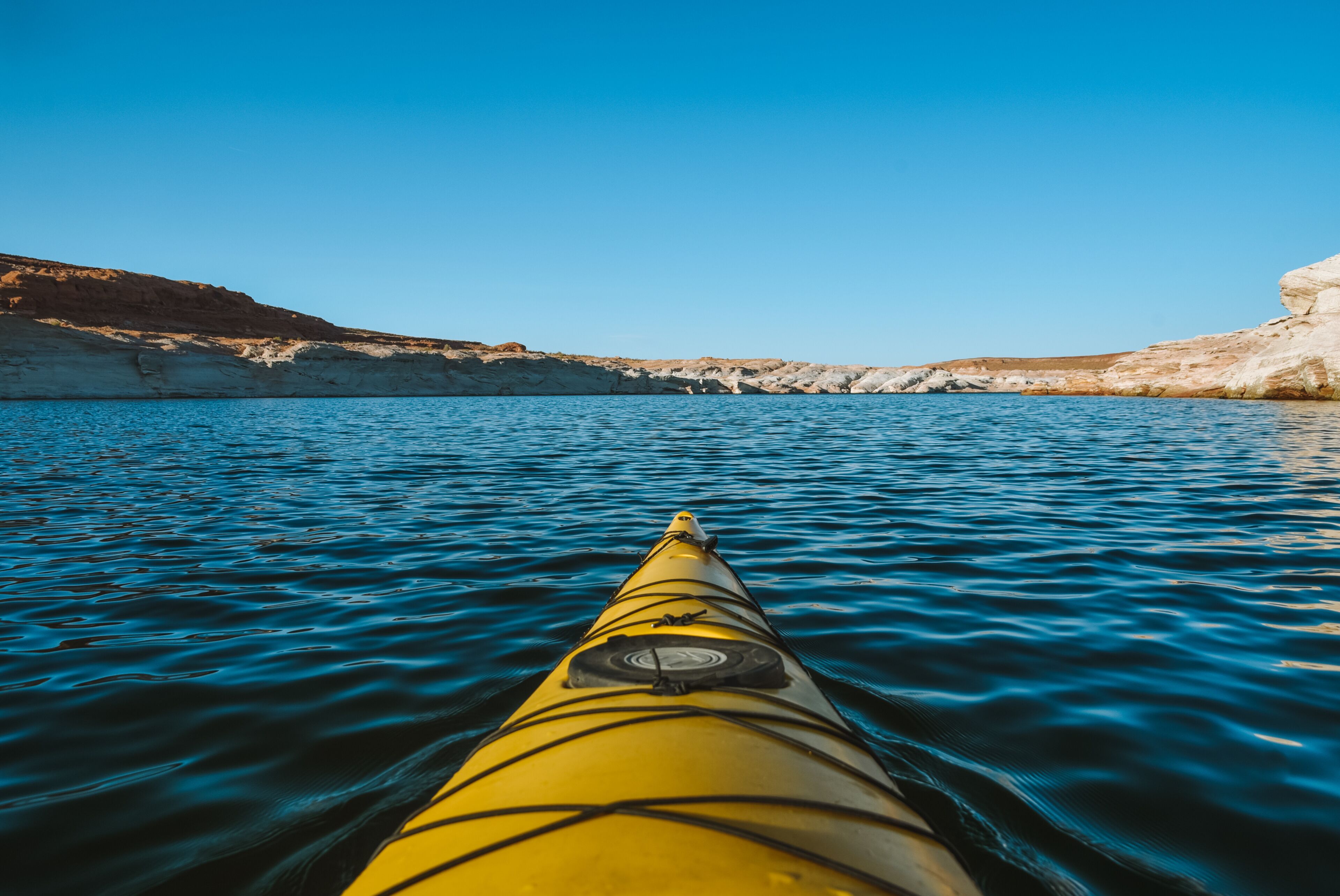 Un kayak amarillo sobre aguas tranquilas, con un cielo azul despejado y acantilados rocosos al fondo.