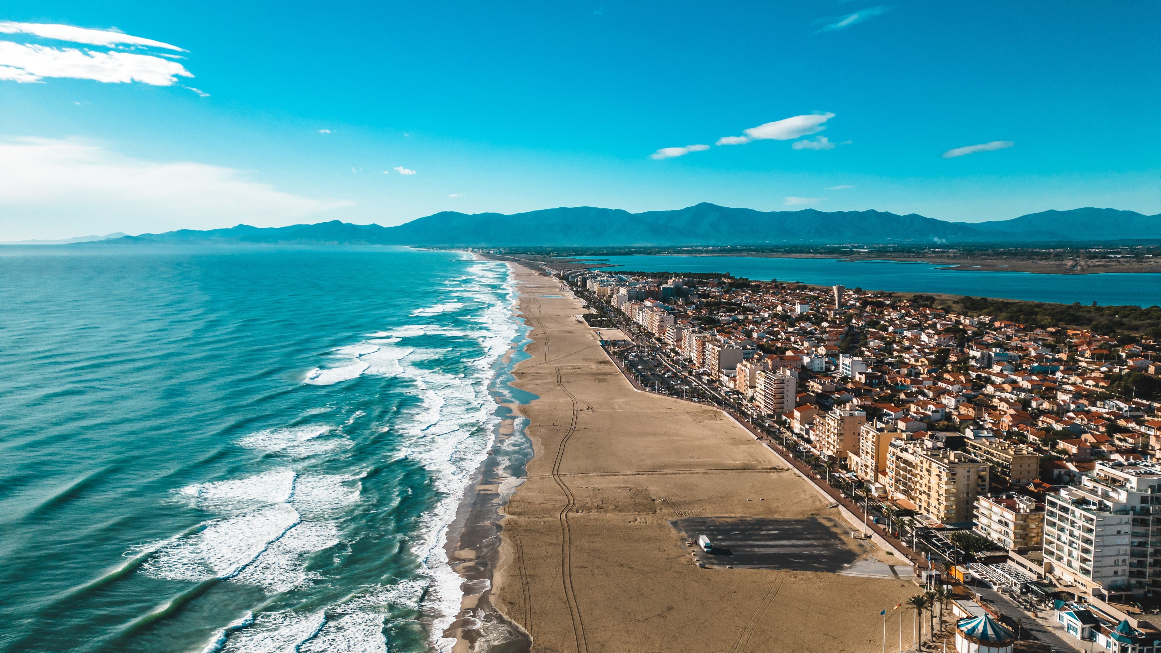 A coastal city with a beach, buildings, and mountains in the background.