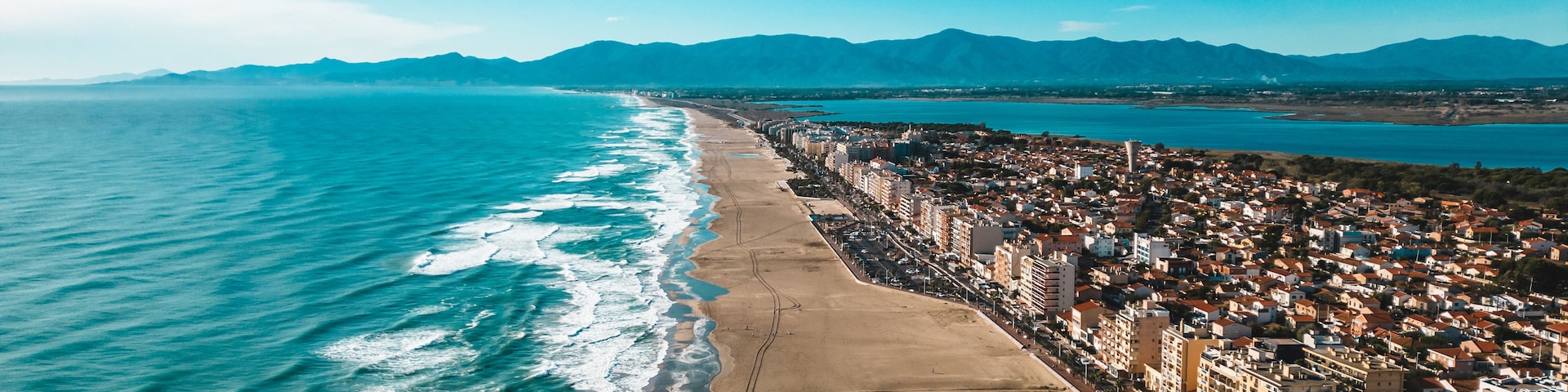 Una ciudad costera con playa, edificios y montañas al fondo.