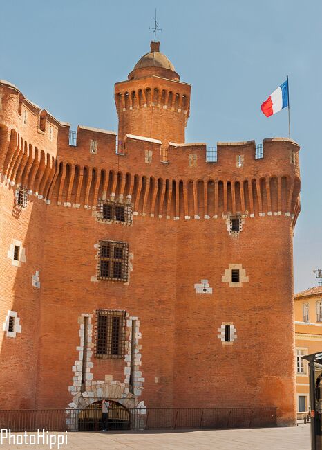 A red brick castle with a flag, a tower, and a gate.