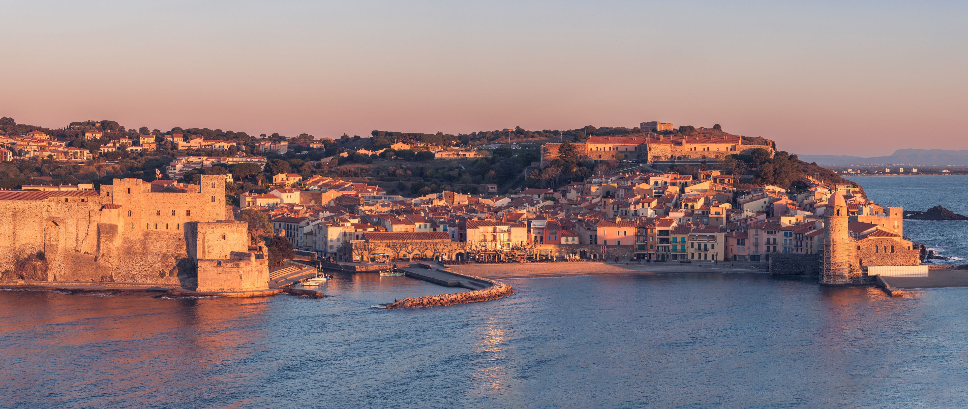 A coastal town with historic buildings, a fortified wall, and a harbor.