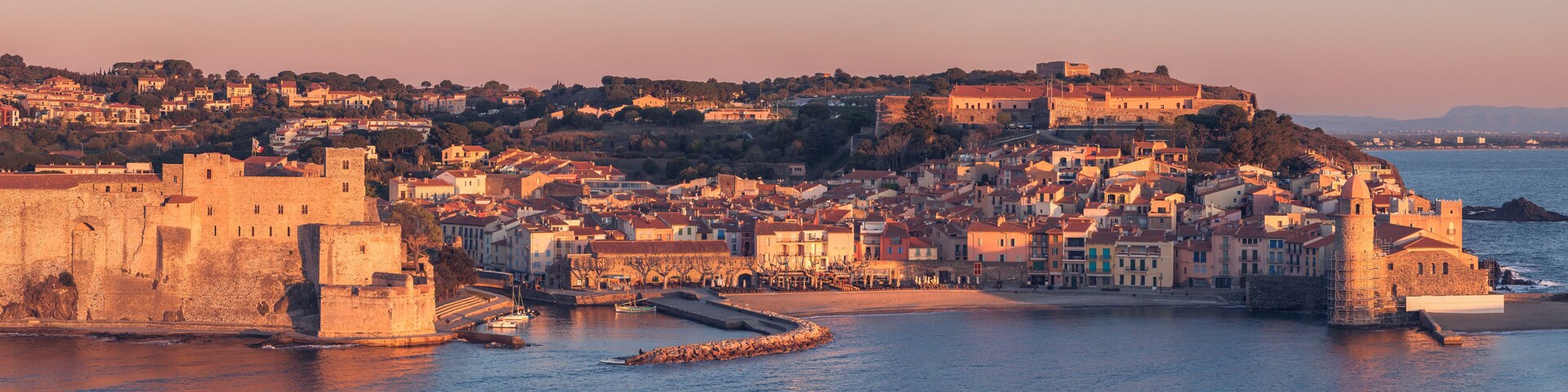 Un pueblo costero con edificios históricos, una muralla fortificada y un puerto.