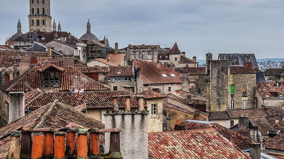 Un paysage urbain historique, caractérisé par une tour imposante et des bâtiments densément regroupés, coiffés de toits en tuiles rouges.