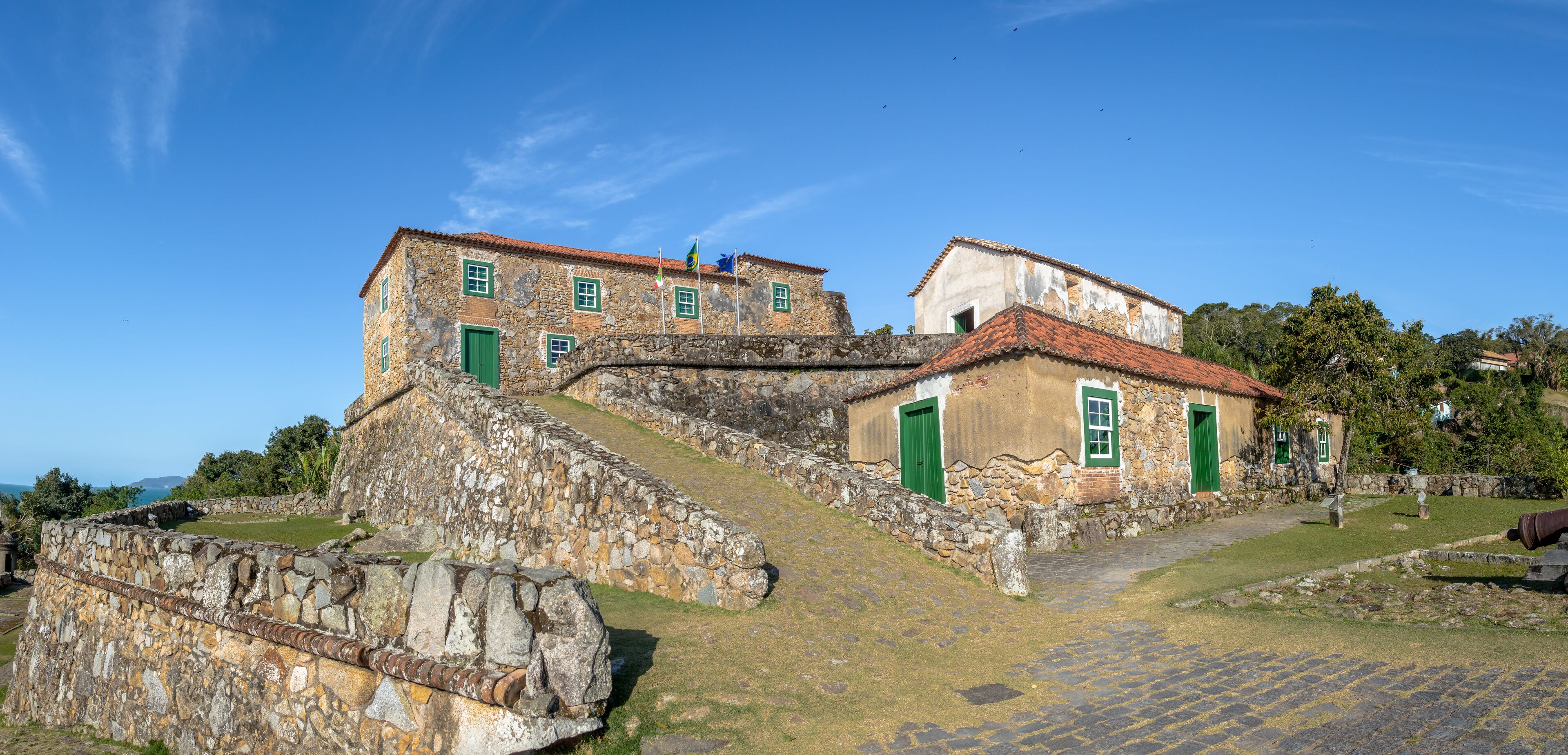A historic stone building with green doors and windows, a cobblestone pathway, and a stone wall.