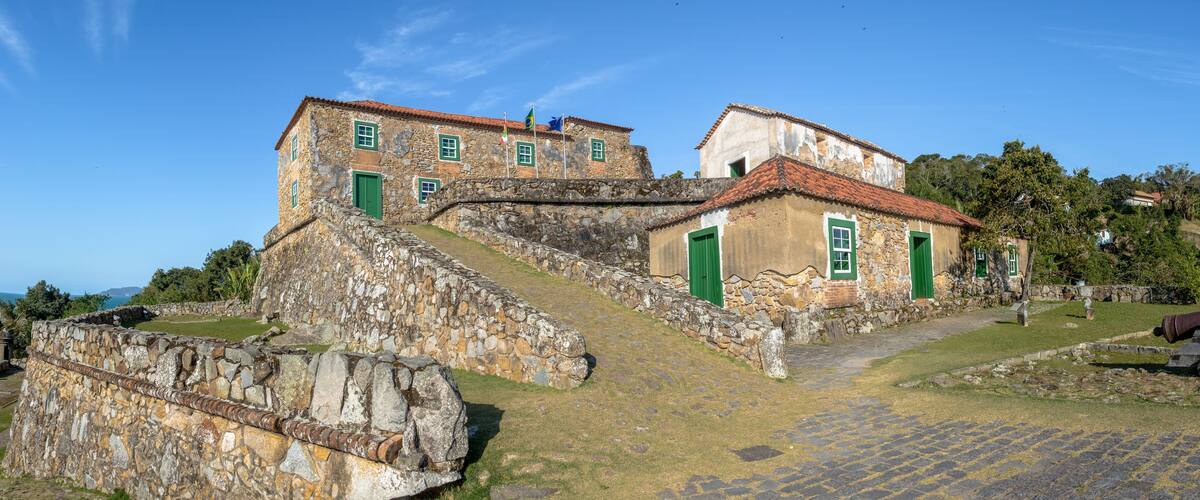 A historic stone building with green doors and windows, a cobblestone pathway, and a stone wall.