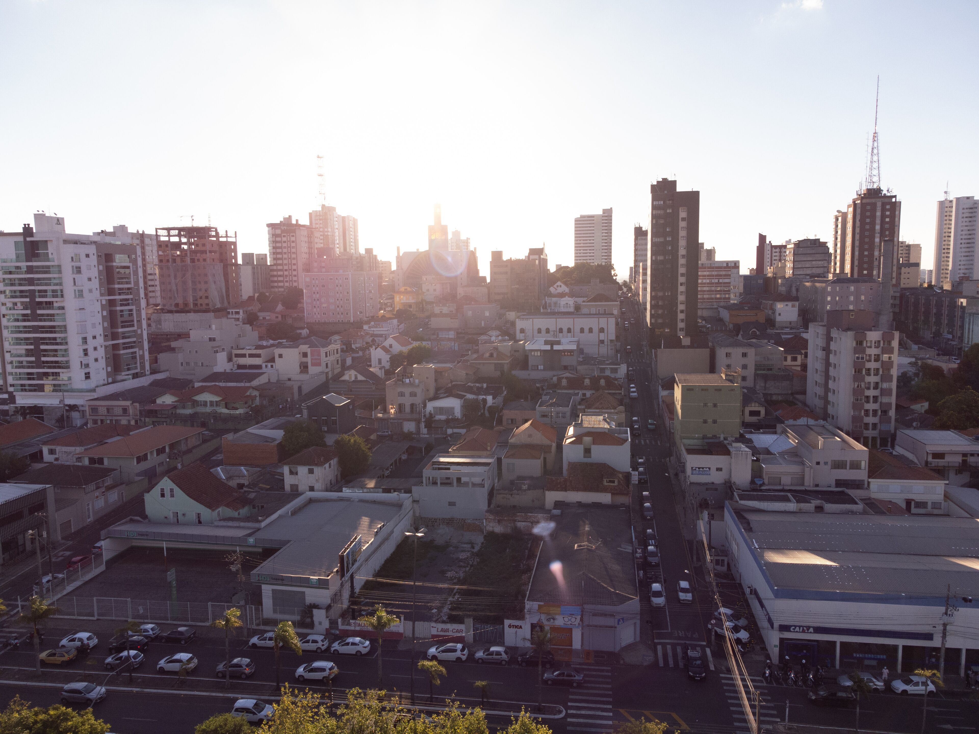 Paisagem urbana com edifícios altos, uma rua movimentada e céu claro.