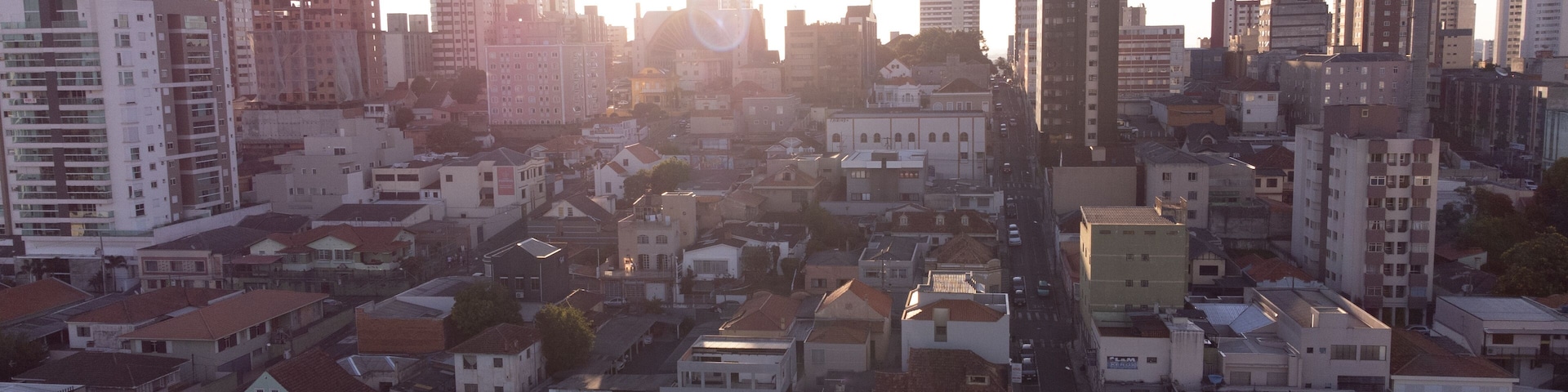 Paisagem urbana com edifícios altos, uma rua movimentada e céu claro.