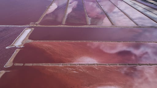 Aerial view of vibrant pink and red salt ponds mirroring the sky, creating a surreal and colorful tapestry, Port Hedland, Australia.
