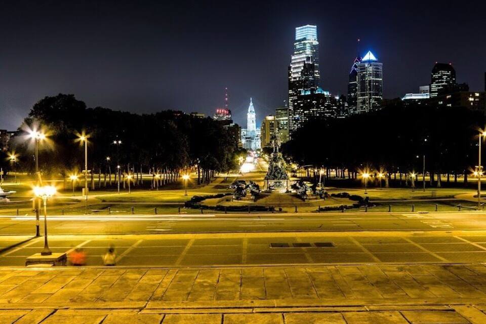 A nighttime cityscape with illuminated skyscrapers, a central monument, and a well-lit park area.