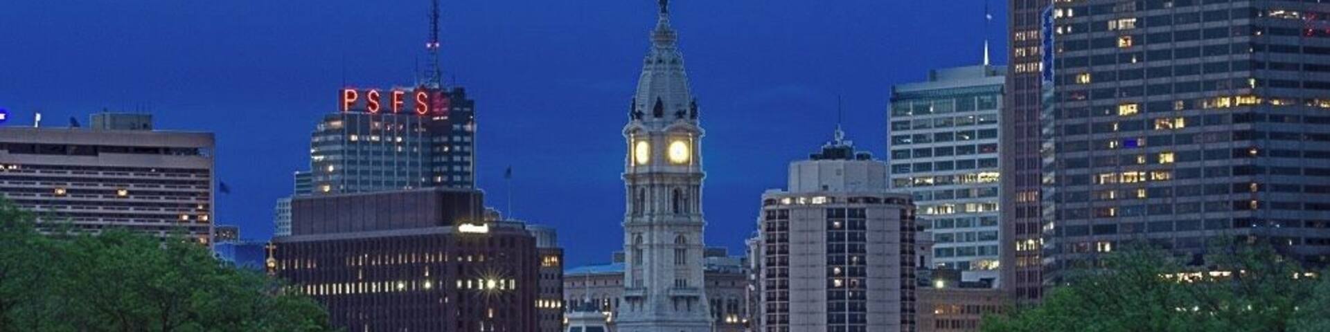 A cityscape with a prominent clock tower, a statue-lined avenue, and modern skyscrapers.