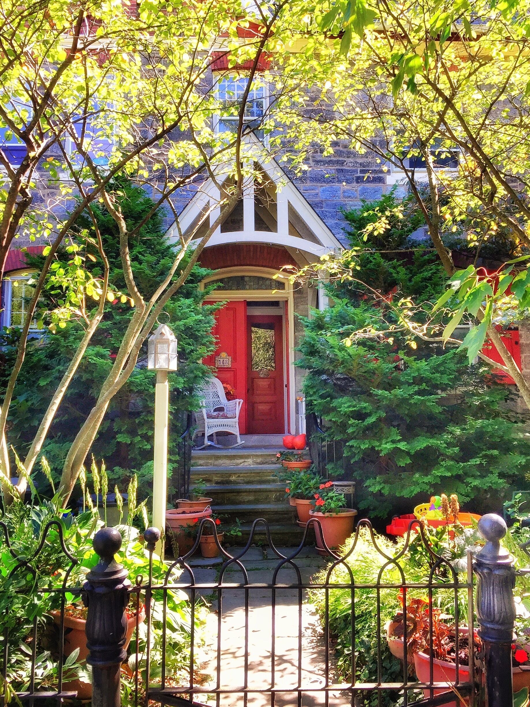 A garden with a red door, white chair, and potted plants.
