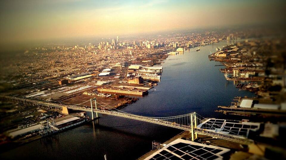 An aerial view of a city with a prominent river, a large bridge, and industrial areas.