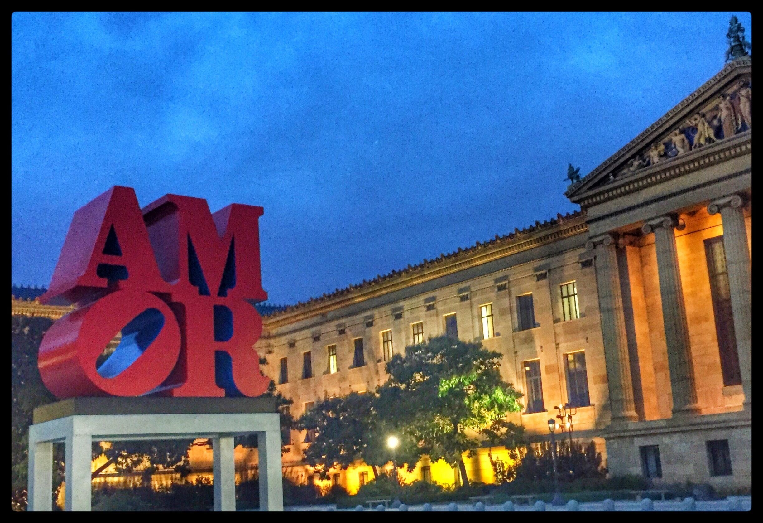 A large red 'AMOR' sign in front of a classical building with columns and a statue on top.