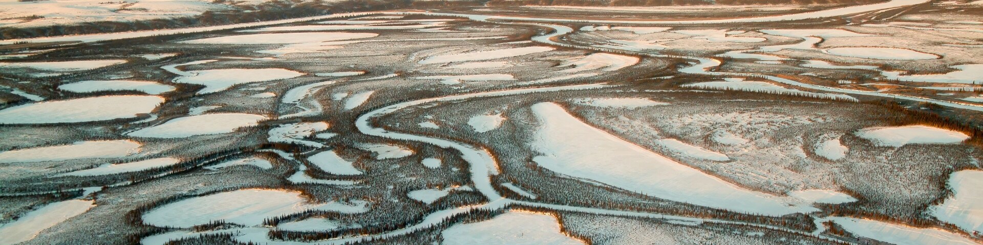 A vast landscape of snow-covered terrain with distinct patterns of water bodies and forested areas.