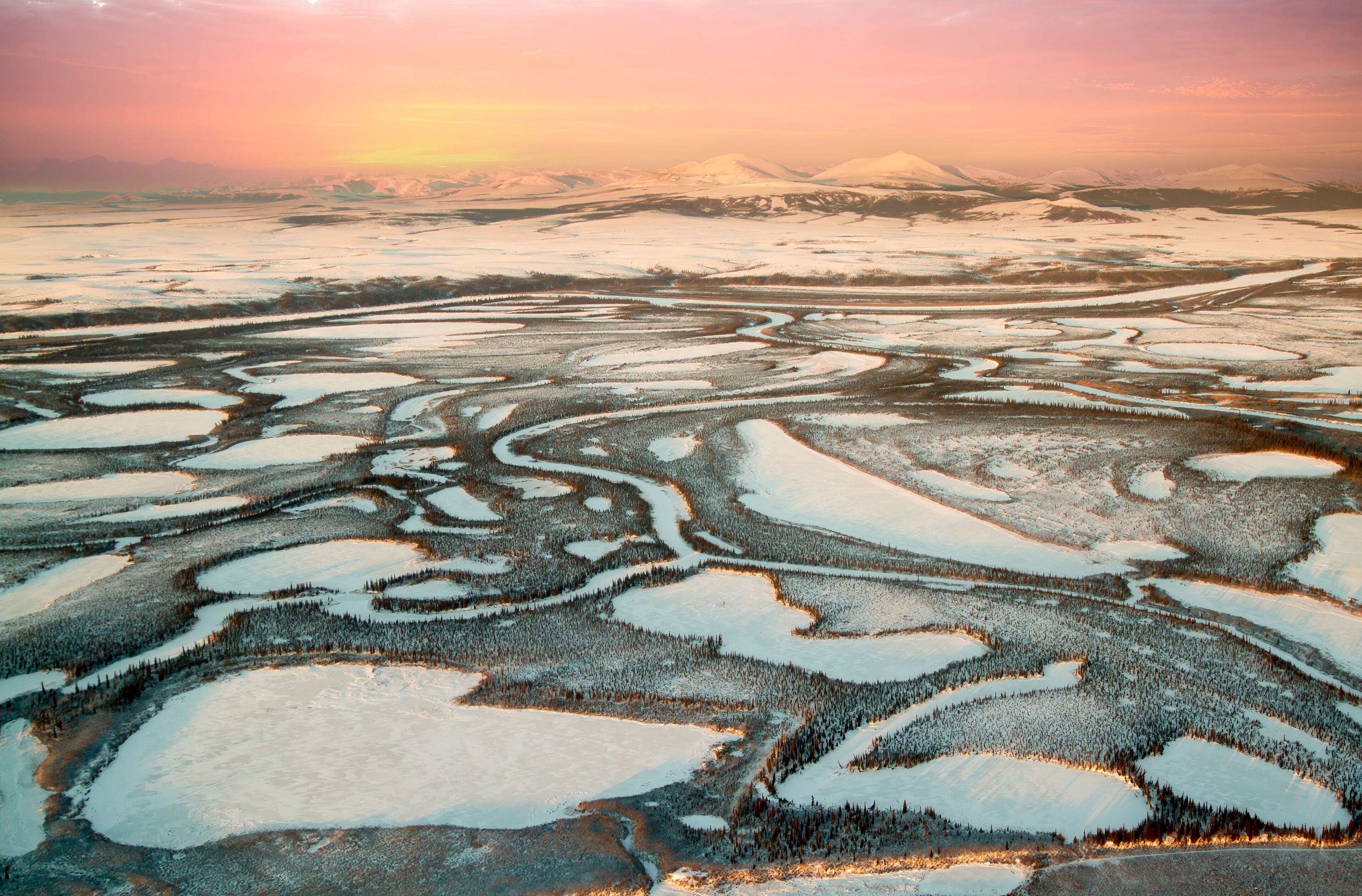 A vast landscape of snow-covered terrain with distinct patterns of water bodies and forested areas.