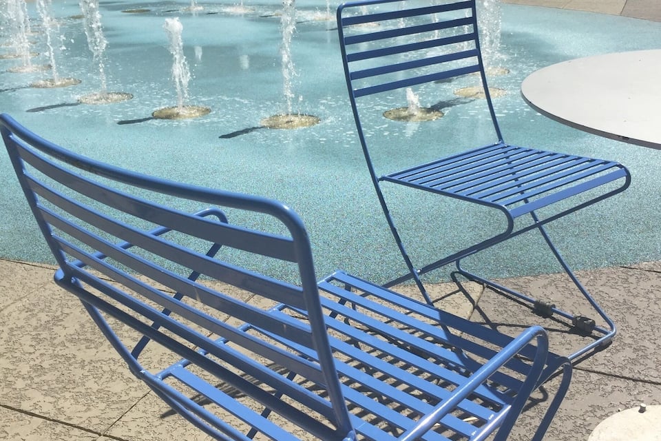 Un banc en métal bleu et une fontaine dans une place publique.