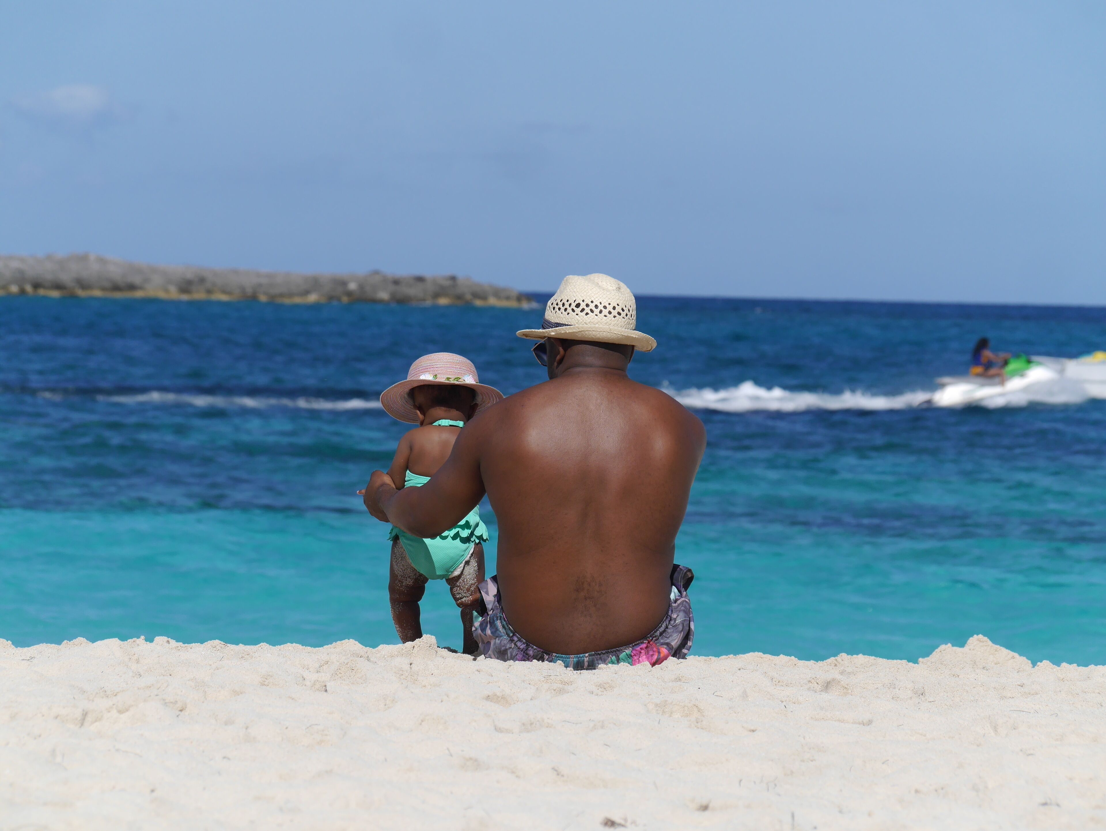 A beach with clear blue water, a sandy shore, and a distant rocky outcrop.