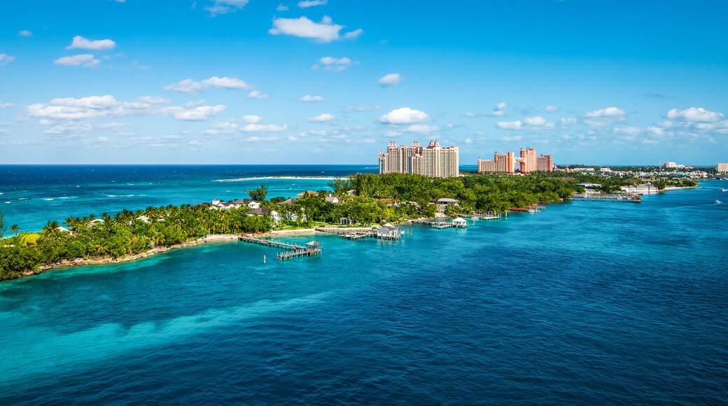 A tropical island with clear turquoise waters, a pier, and high-rise hotels in the background.