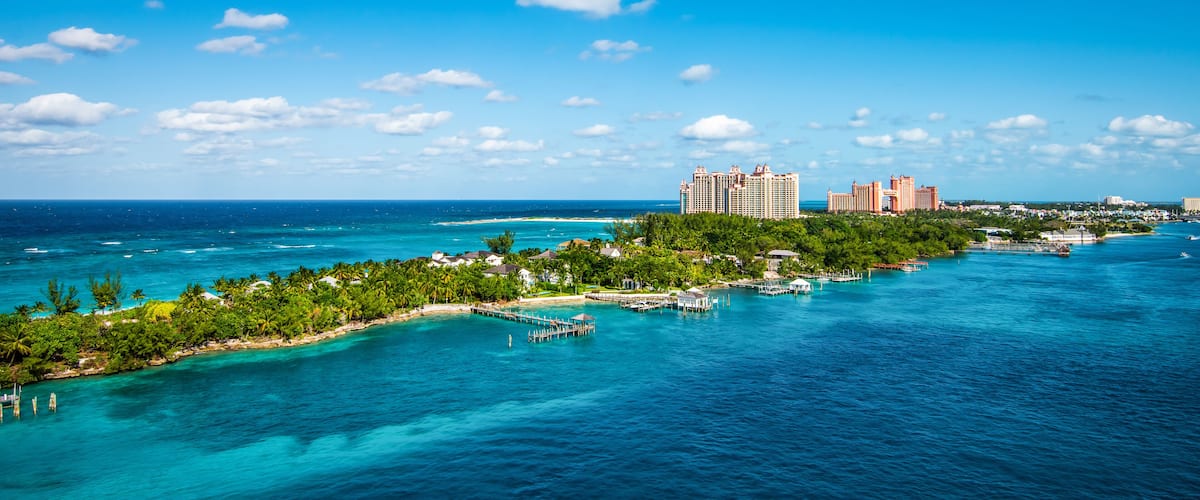 A tropical island with clear turquoise waters, a pier, and high-rise hotels in the background.