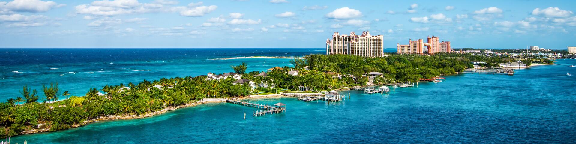 A tropical island with clear turquoise waters, a pier, and high-rise hotels in the background.