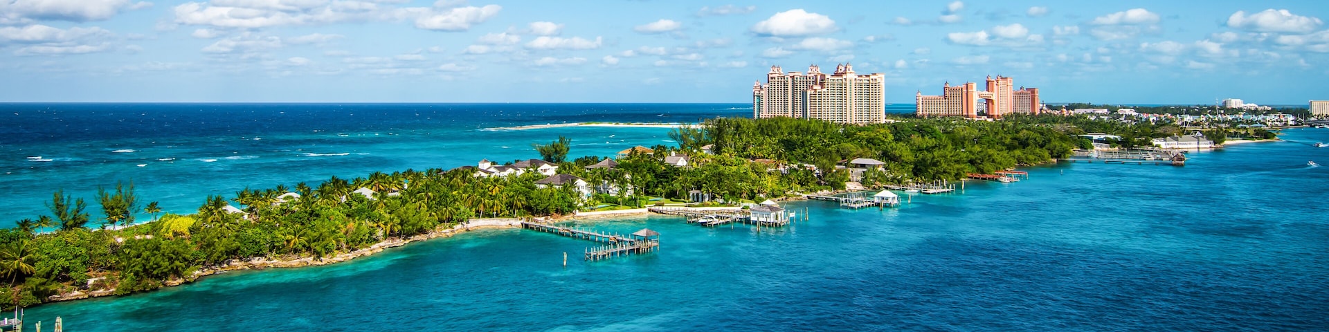 A tropical island with clear turquoise waters, a pier, and high-rise hotels in the background.