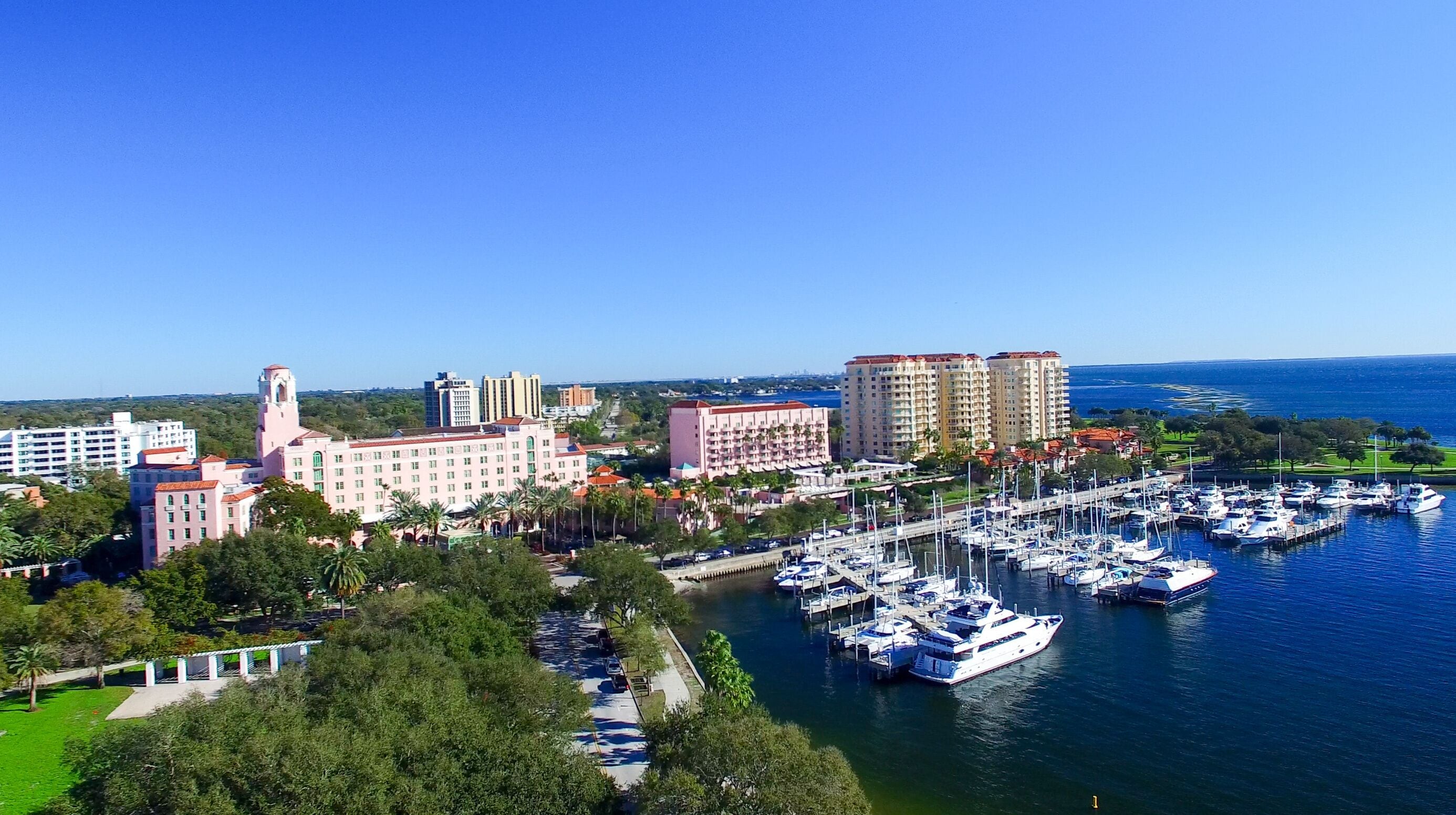 A marina with numerous boats docked, surrounded by buildings and palm trees.