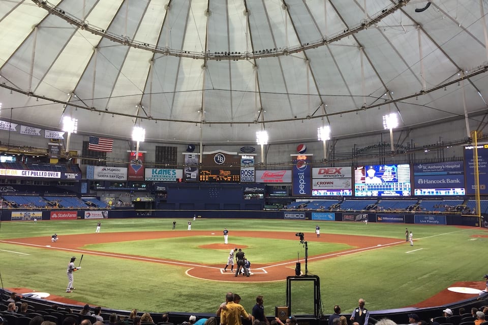 Um estádio de beisebol com uma grande área de assentos coberta e diversos anúncios nas paredes.