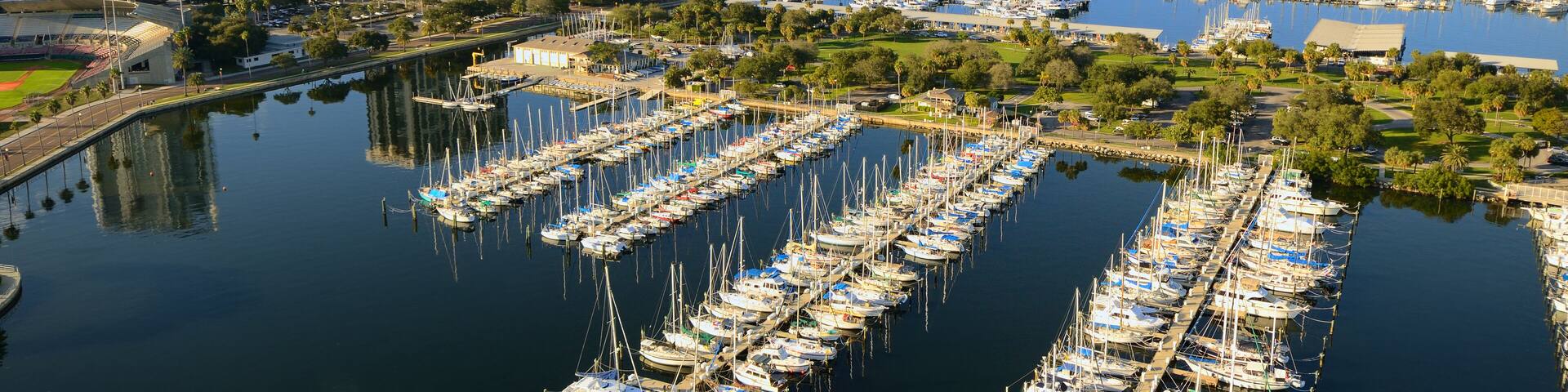 A marina with numerous boats docked, surrounded by city buildings and greenery.