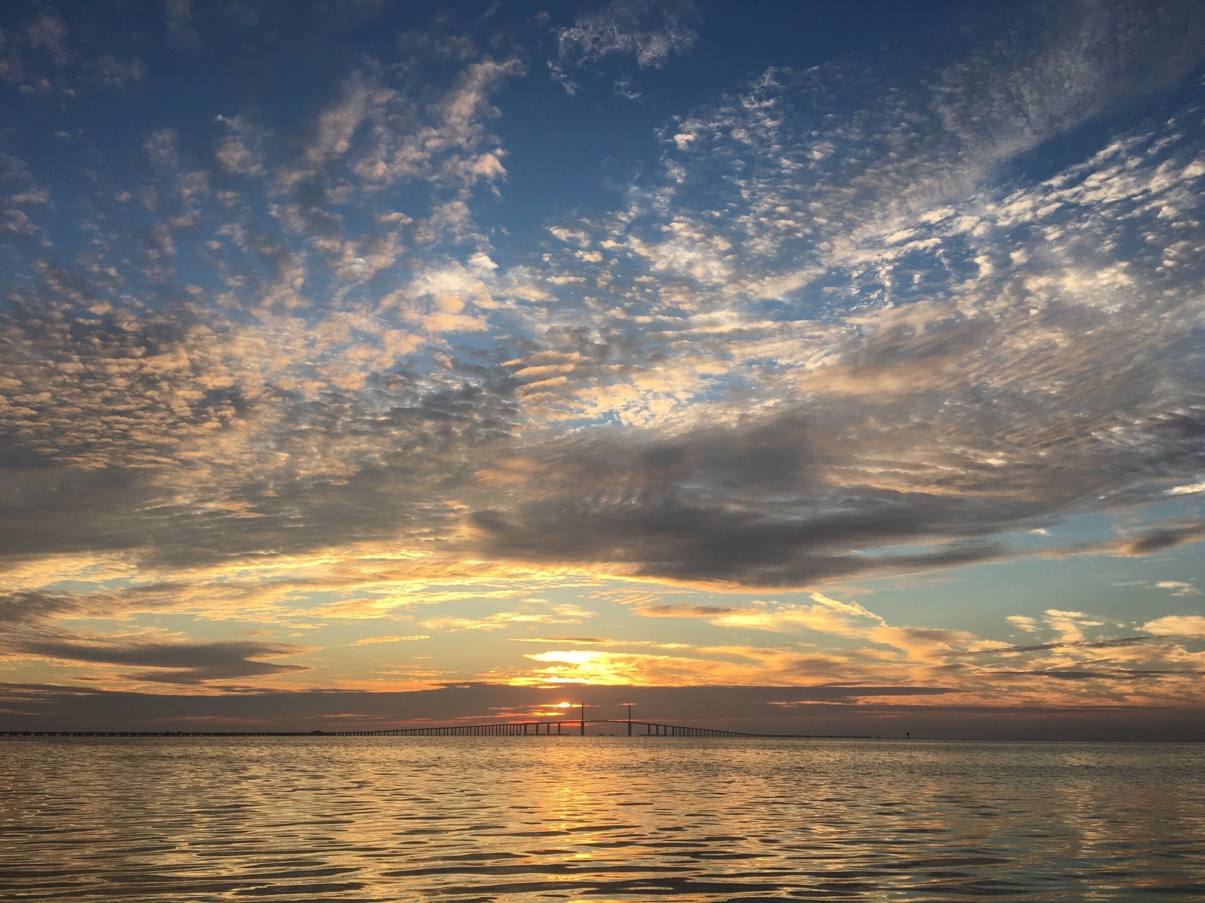 A sunset over a body of water with a bridge in the distance.