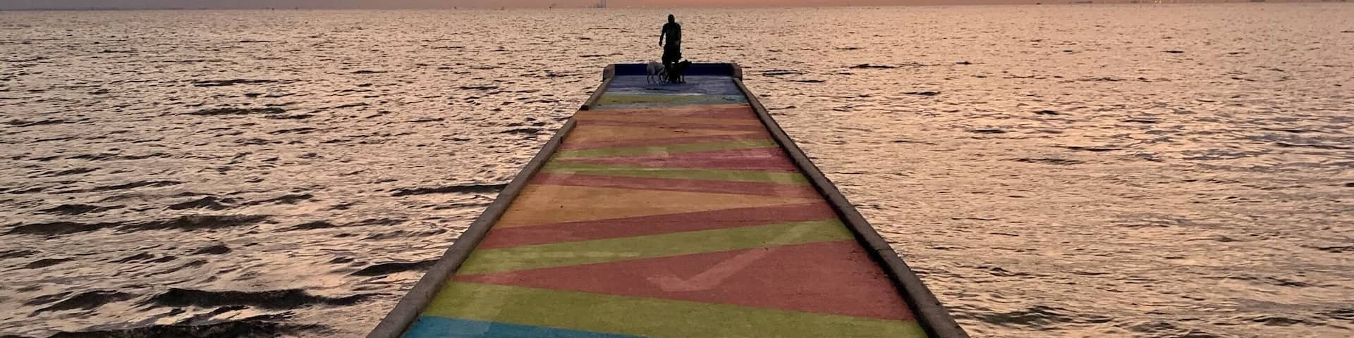 A pier extending into calm waters with a colorful striped walkway.