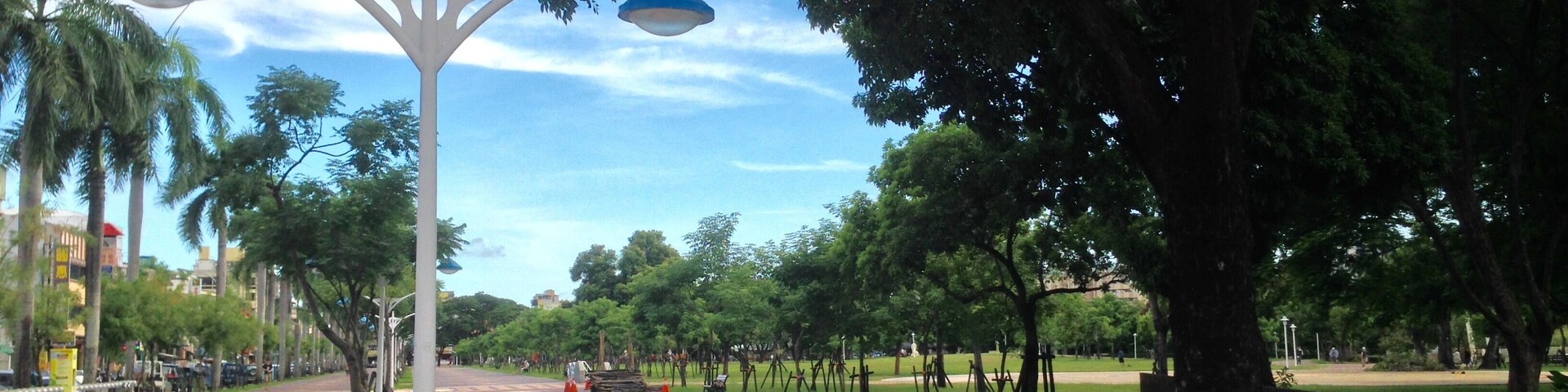 Un parque con un farol blanco, árboles y un sendero pavimentado.