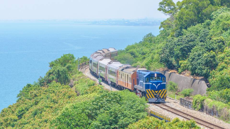 A train traveling along a track surrounded by lush greenery and overlooking a body of water.