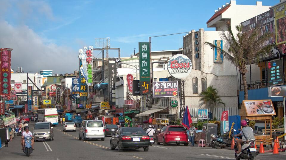 A busy street with various shops and signs, including a Coors Light sign and a sign for a pub.