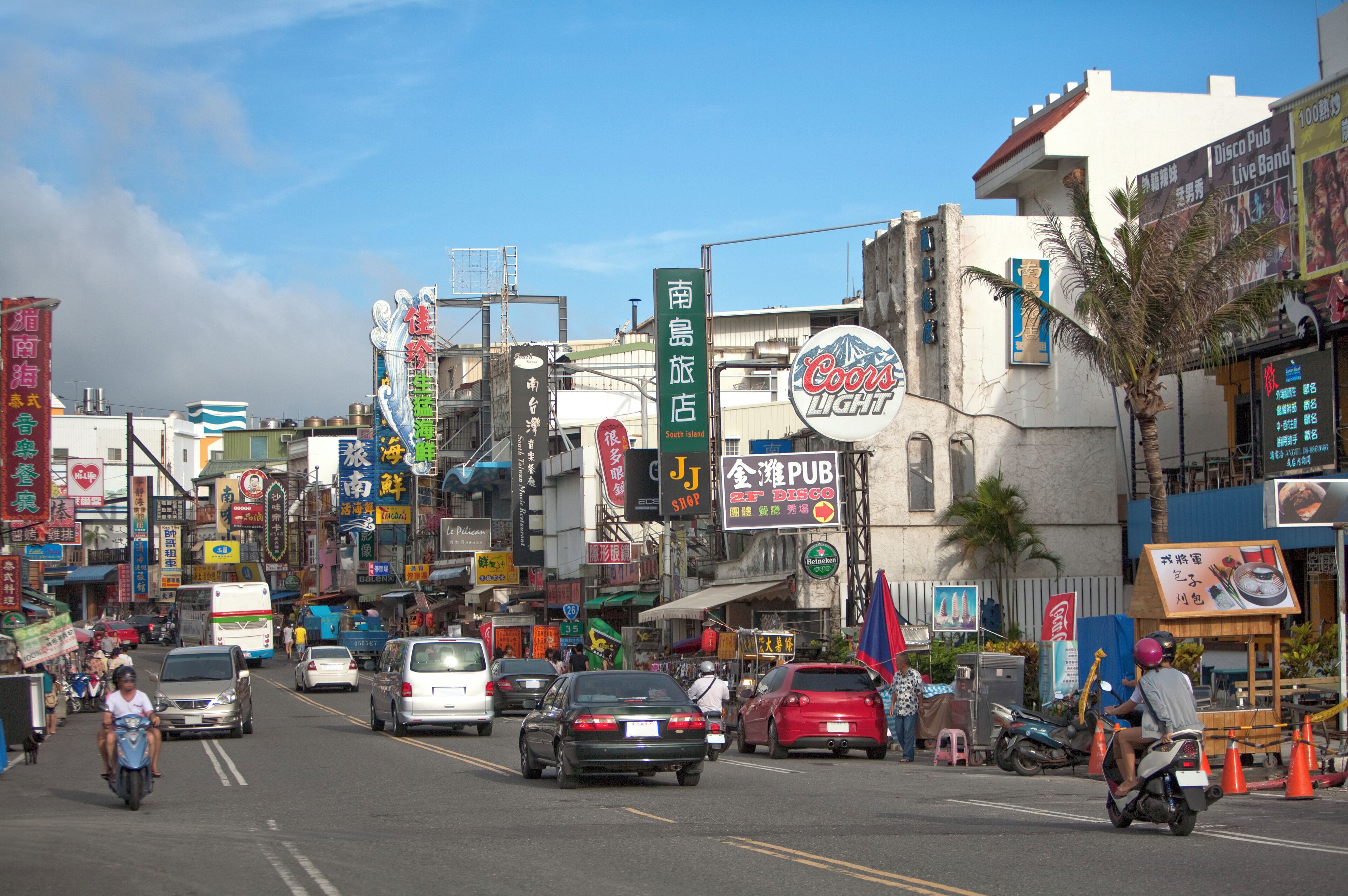 A busy street with various shops and signs, including a Coors Light sign and a sign for a pub.