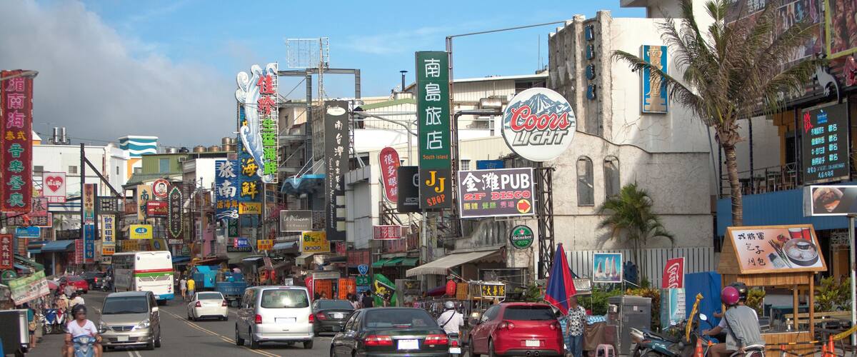 A busy street with various shops and signs, including a Coors Light sign and a sign for a pub.