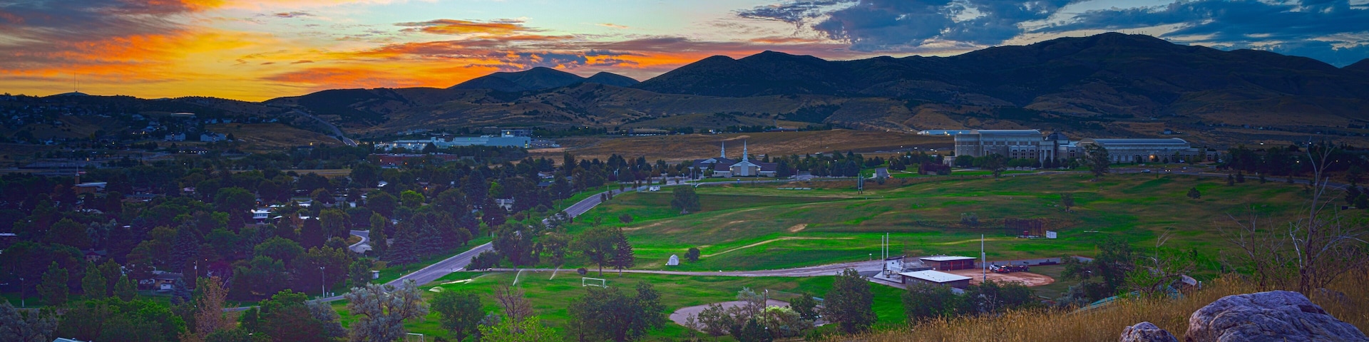A sunset over a rural landscape with mountains, a church, and a large building.