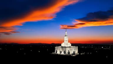 A large, illuminated building with a spire, surrounded by a cityscape at sunset.
