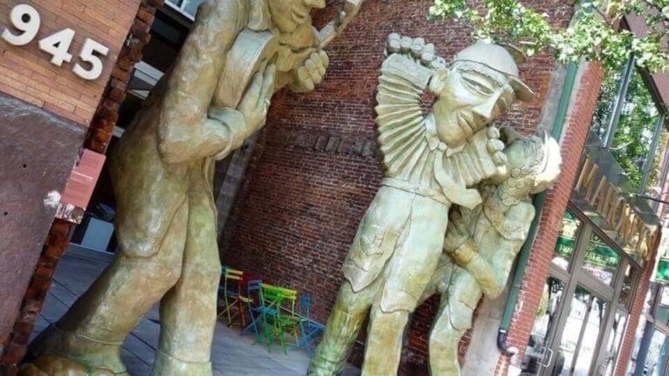 A street scene with a large bronze sculpture of a man playing a trumpet and a child.
