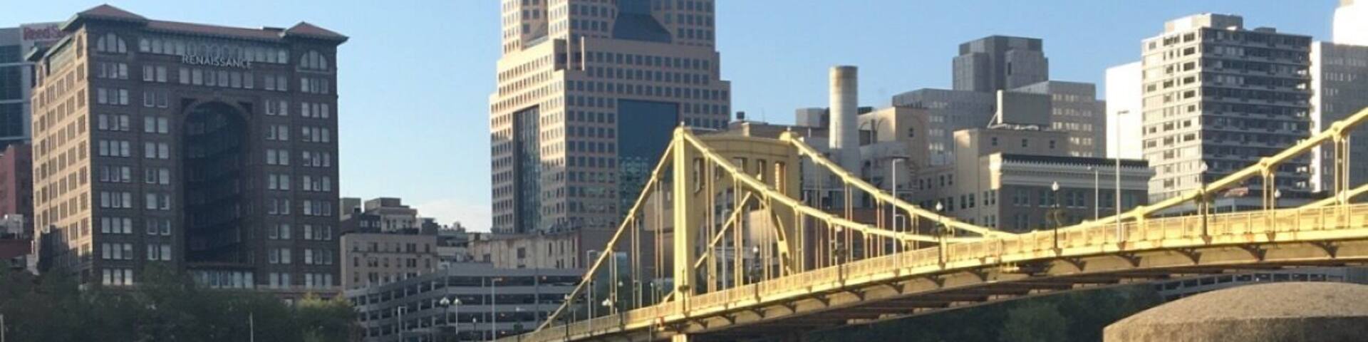 A river with a chain barrier, a yellow bridge, and a city skyline with tall buildings.