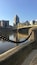 A river with a chain barrier, a yellow bridge, and a city skyline with tall buildings.