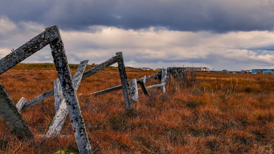 A rustic wooden fence in a field with a cloudy sky.