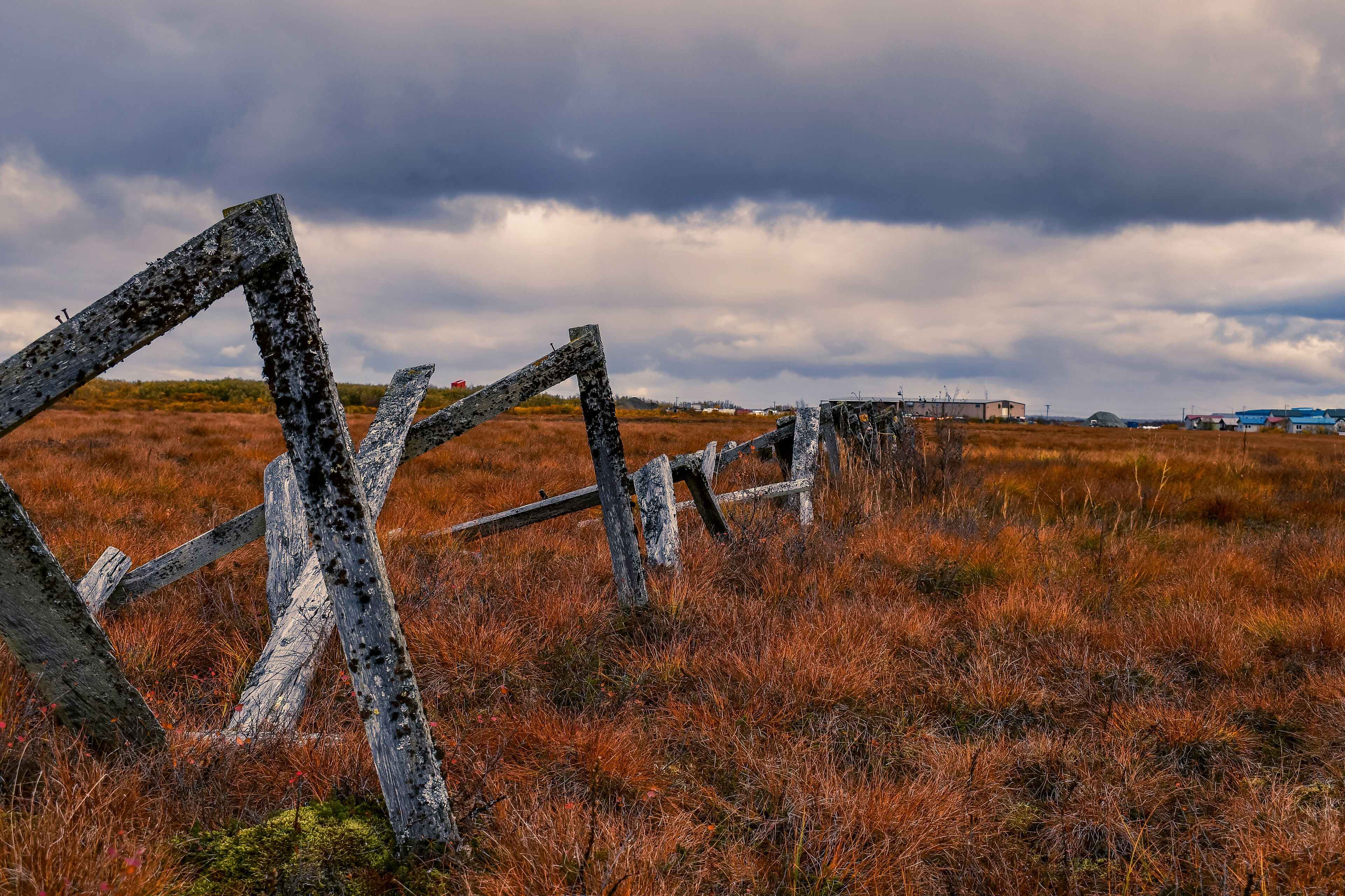 A rustic wooden fence in a field with a cloudy sky.