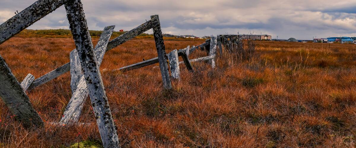 A rustic wooden fence in a field with a cloudy sky.
