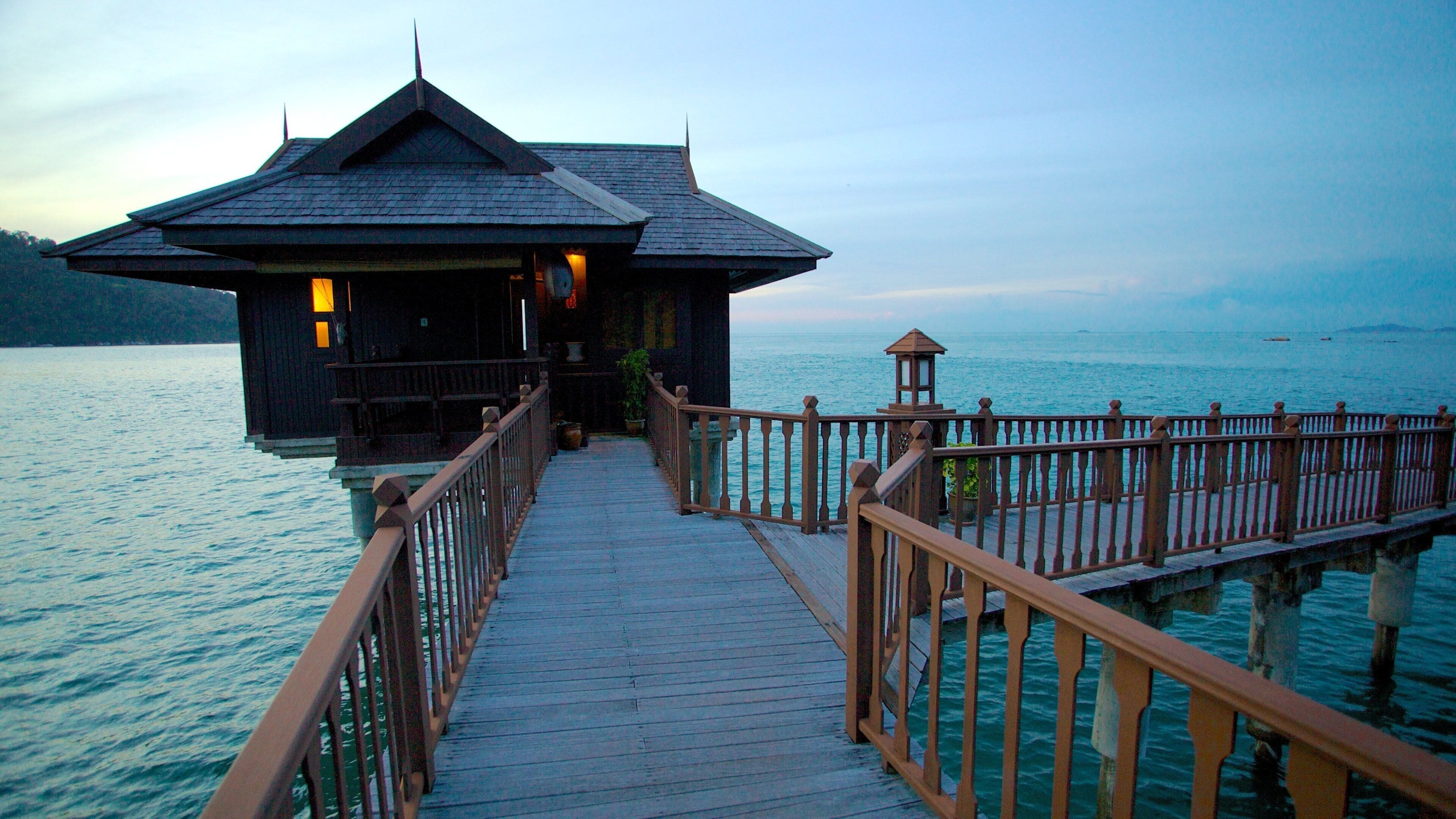A wooden pier leading to a dark-roofed building with a lantern on the right.