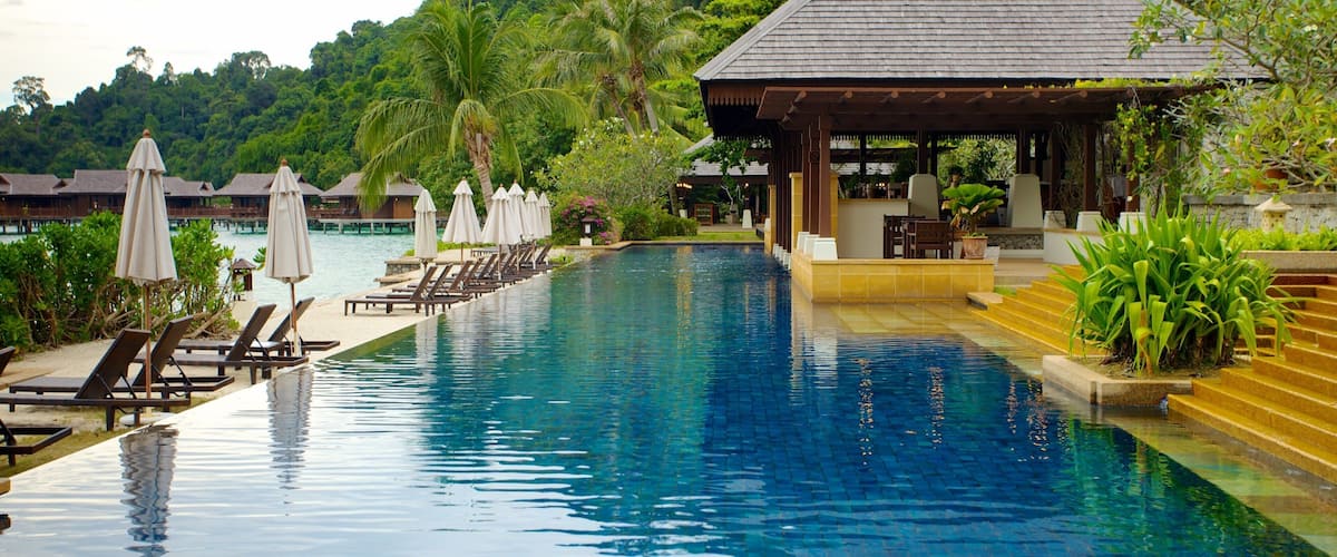 A pool with lounge chairs and umbrellas, a gazebo, and lush greenery in the background.